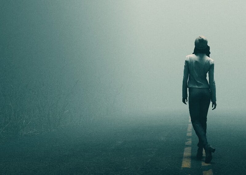 A woman pondering the uncertain journey ahead, representing the effects of drug abuse, as she gazes down a fog-covered road.
