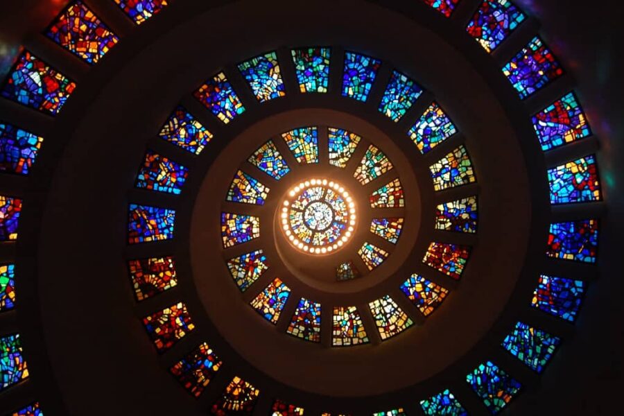 A spiral staircase with vibrant stained glass windows, symbolizing growth and embodying the theme 'progress, not perfection'.