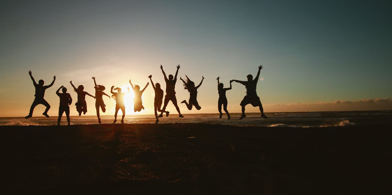Diverse friends jumping joyfully on a beach, capturing the essence of 'progress, not perfection' in a moment of shared happiness.