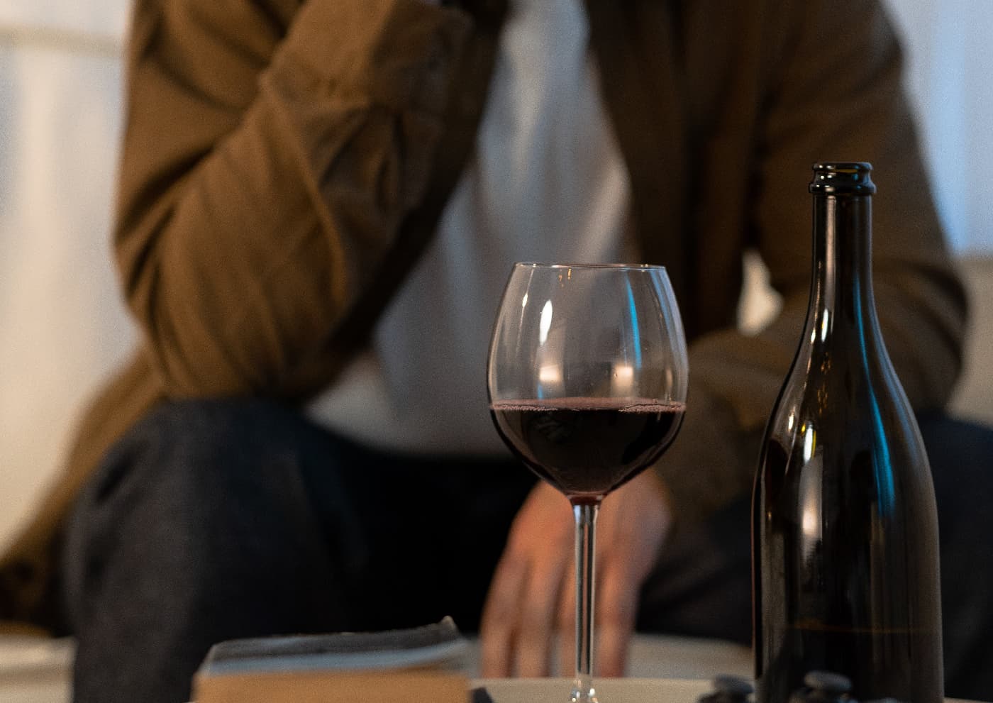 A close-up of a wine bottle in the foreground with a blurred figure of a man in the background, symbolizing the struggle and distance from alcohol faced during the journey of overcoming alcohol withdrawals.
