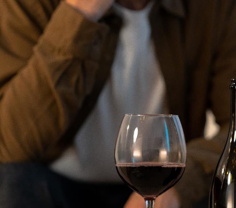 Close-up of a glass of wine with a blurry man in the background, highlighting the focus on alcohol over personal relationships, related to the characteristics of alcoholism.