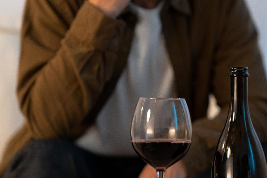 Close-up of a glass of wine with a blurry man in the background, highlighting the focus on alcohol over personal relationships, related to the characteristics of alcoholism.