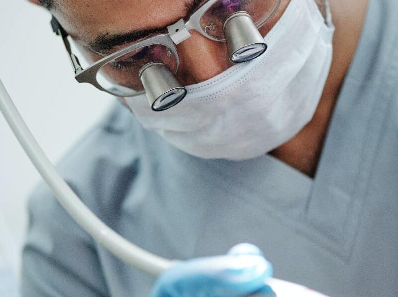 Dentist in protective gear examining and treating damaged teeth, representing the dental care for meth mouth, with dental tools in foreground.