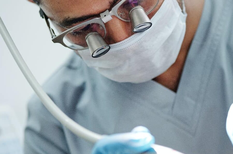 Dentist in protective gear examining and treating damaged teeth, representing the dental care for meth mouth, with dental tools in foreground.