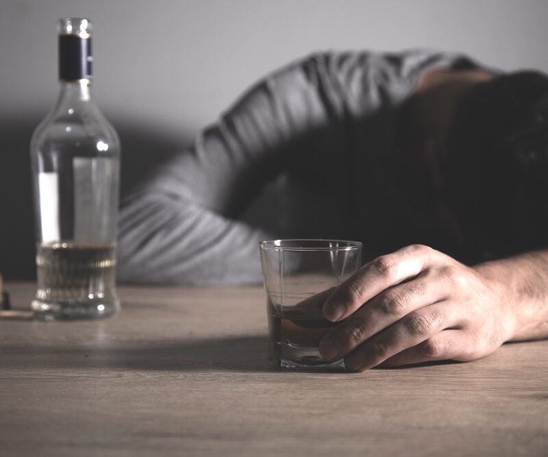 Drunk man holding a glass of alcohol fell asleep on a table surface