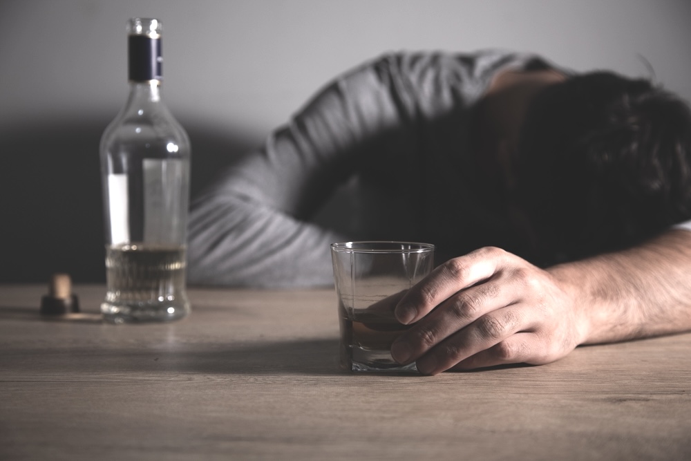 Drunk man holding a glass of alcohol fell asleep on a table surface
